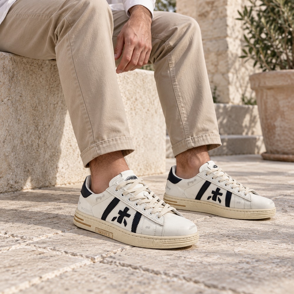 Ambientación con IA: Zapatillas Premiata Russell de hombre en blanco y negro, puesto con pantalones.