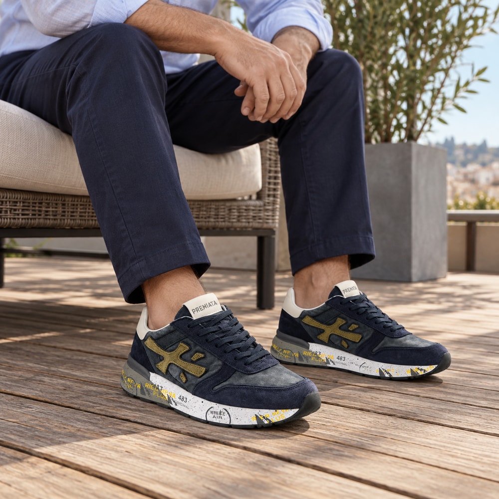 Ambientación con IA: Zapatillas Premiata Mick de hombre en azul y naranja, puesto con pantalones.