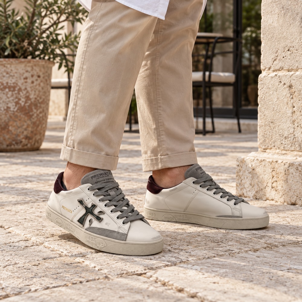 Ambientación con IA: Zapatillas Premiata Steven de hombre en blanco y burdeos, puesto con pantalones.