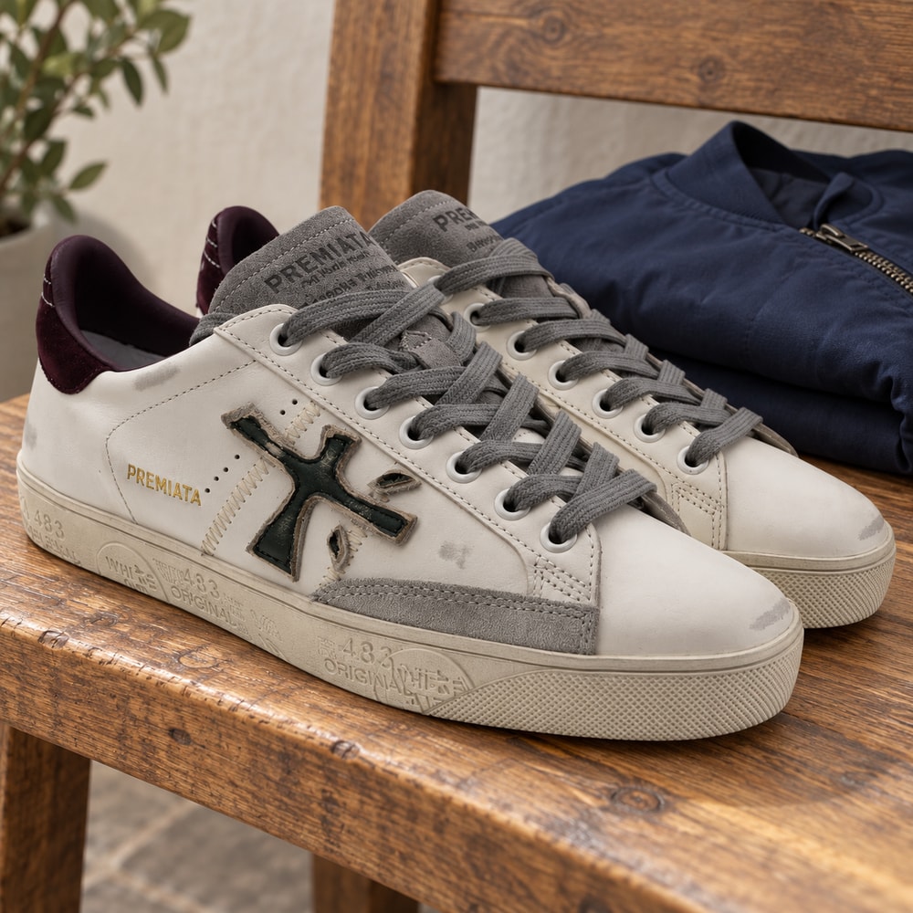 Ambientación con IA: Zapatillas Premiata Steven de hombre en blanco y burdeos, junto a prendas lisas.