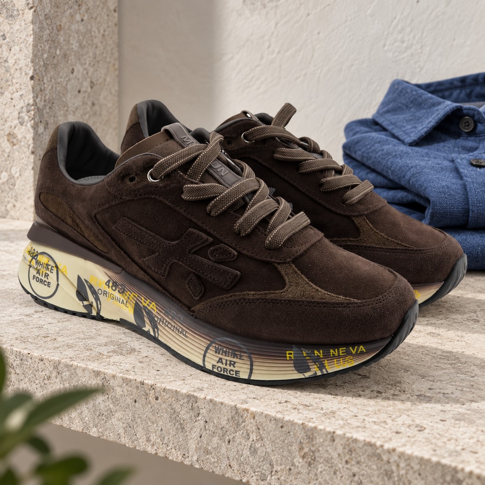 Ambientación con IA: Zapatillas Premiata Moerun de hombre en color chocolate, junto a prendas lisas.