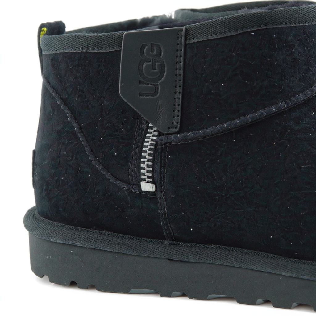 Detalle técnico de la bota UGG negra, mostrando la textura del exterior Nubuck, el forro de cordero, las costuras precisas y la suela microporosa.
